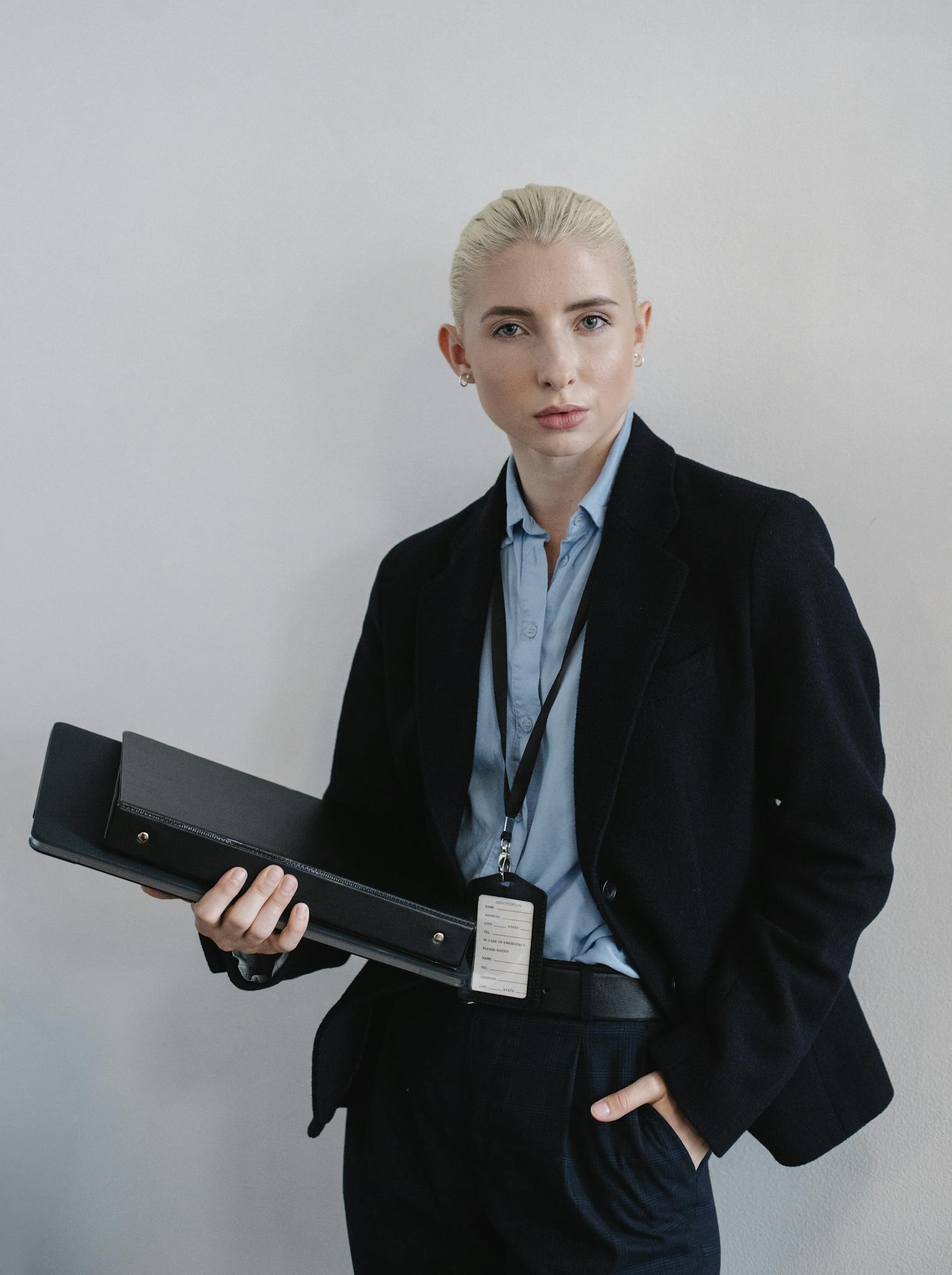 Confident businesswoman in formal attire holding a black folder indoors.